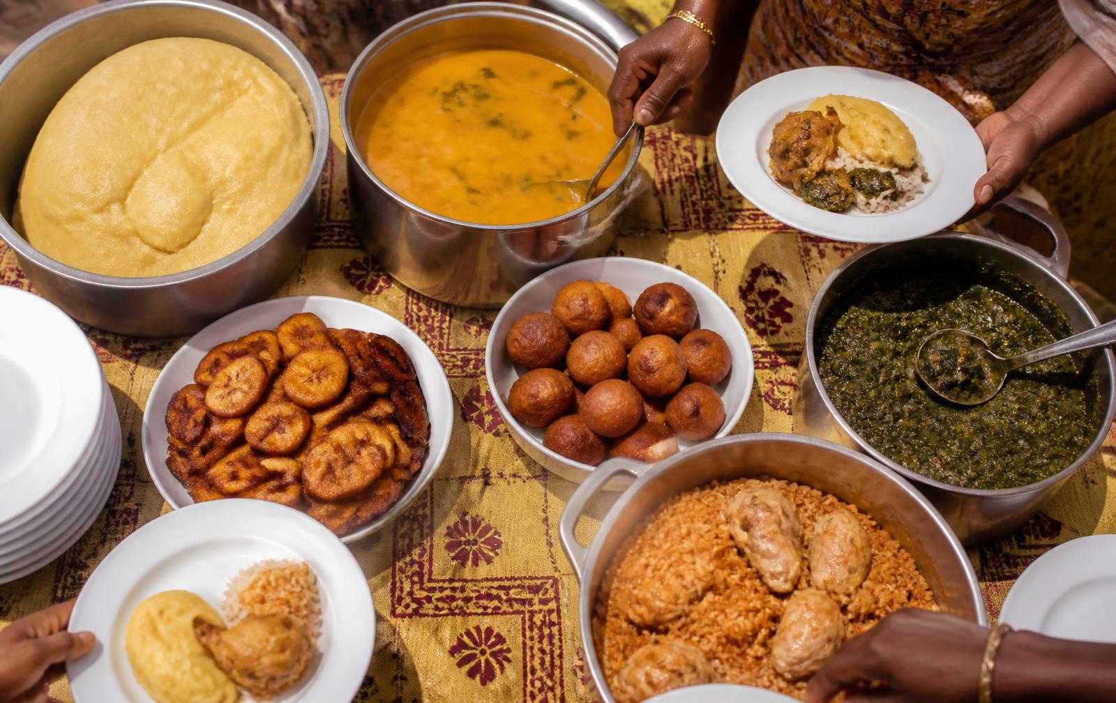 Pots of achu, corn fufu, njama njama, kati kati, plantain and puff puff being served